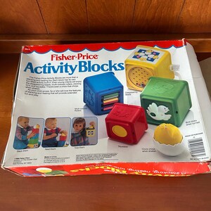 May include: A Fisher-Price Activity Blocks toy set. The box is red and white with the words "Activity Blocks" in large blue letters. The set includes blue, yellow, red, and green blocks with different features, including disappearing beads and a chick that chirps.
