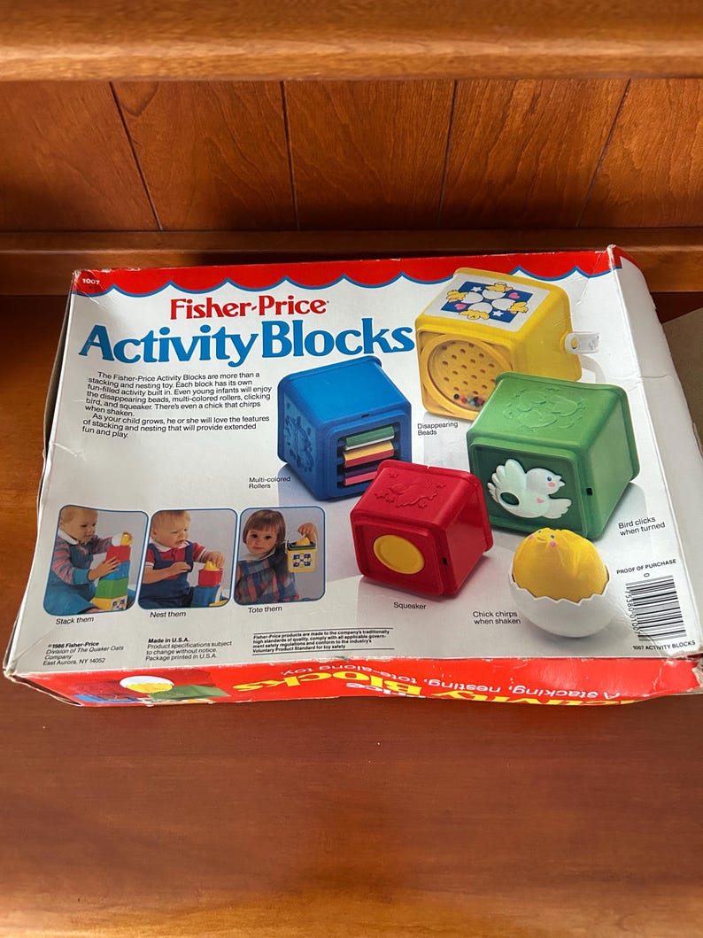 May include: A Fisher-Price Activity Blocks toy set. The box is red and white with the words "Activity Blocks" in large blue letters. The set includes blue, yellow, red, and green blocks with different features, including disappearing beads and a chick that chirps.