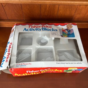 May include: Fisher-Price Activity Blocks toy set in its original packaging. The box is red, white, and blue with the product name and a picture of a child playing with the blocks. The box is designed for children aged 6-30 months.