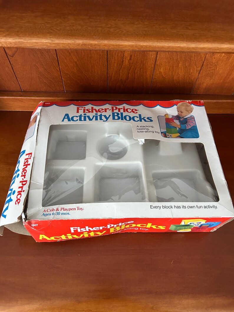 May include: Fisher-Price Activity Blocks toy set in its original packaging. The box is red, white, and blue with the product name and a picture of a child playing with the blocks. The box is designed for children aged 6-30 months.