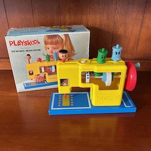 Puede incluir: Juguete de máquina de coser Playskool vintage. La máquina es amarilla con base azul y detalles rojos. La caja muestra a un niño y las palabras "Playskool Sewing Machine". Para niños de 3 a 6 años.