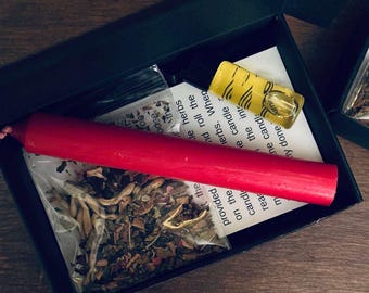 May include: A black box with a red candle, a small bag of dried herbs, a small bottle of oil, and a piece of paper with instructions. The paper says "the provided herbs. When you roll the candle into the herbs, read the candle"