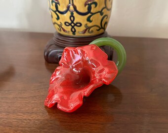 May include: A red glass flower with a green stem. The flower is sitting on a wooden surface.