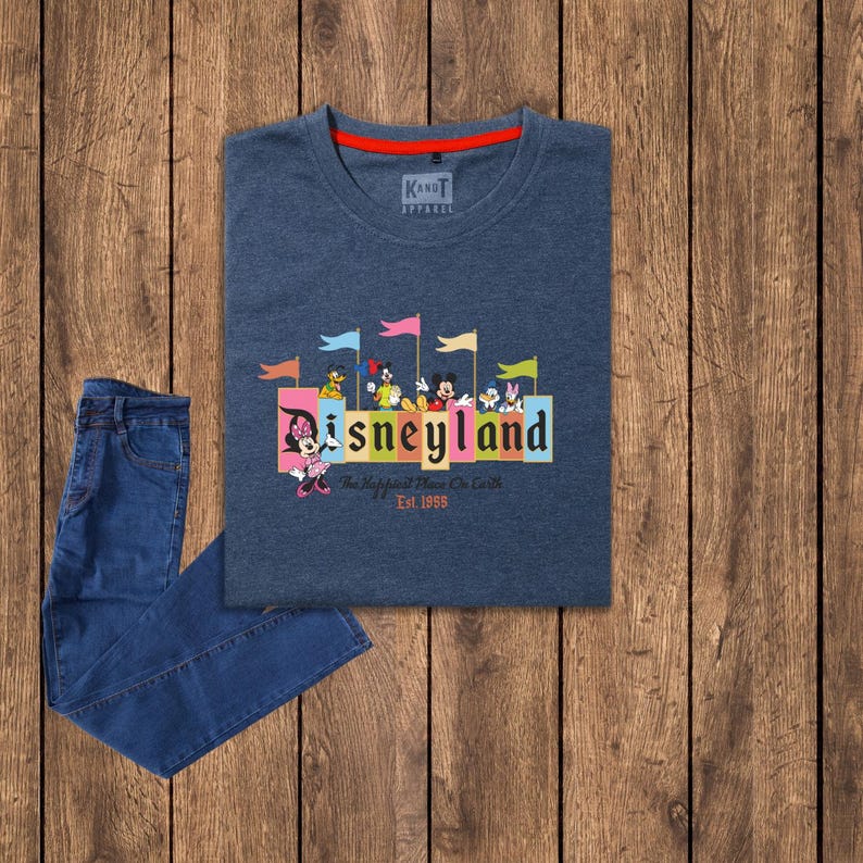 Puede incluir: Una camiseta azul oscuro con un gr&aacute;fico de Disneyland colorido que presenta a Mickey Mouse y otros personajes de Disney. El gr&aacute;fico incluye el texto "Disneyland" y "The Happiest Place On Earth" con el a&ntilde;o "Est. 1955".