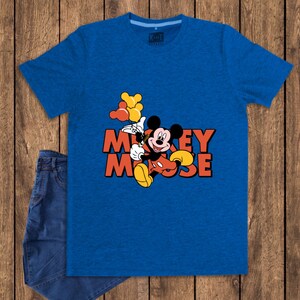 May include: A blue t-shirt featuring a graphic of Mickey Mouse holding balloons. The text "Mickey Mouse" is in orange and black. A pair of blue jeans is partially visible on a wooden background.