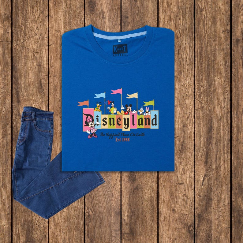 Puede incluir: Una camiseta azul con un gr&aacute;fico de Disneyland colorido que presenta a Mickey Mouse y otros personajes de Disney. El gr&aacute;fico incluye el texto "Disneyland" y "The Happiest Place On Earth" con el a&ntilde;o "Est. 1955".