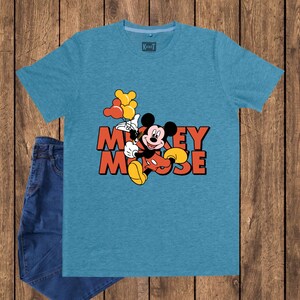 May include: A turquoise t-shirt featuring a graphic of Mickey Mouse holding balloons, with the words "Mickey Mouse" in orange. The shirt is paired with blue jeans. The shirt has a tag that says "Karot".