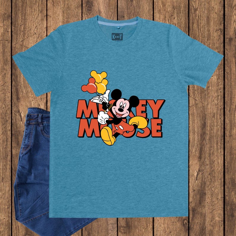 May include: A turquoise t-shirt featuring a graphic of Mickey Mouse holding balloons, with the words "Mickey Mouse" in orange. The shirt is paired with blue jeans. The shirt has a tag that says "Karot".