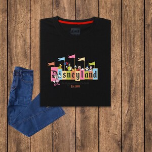 Puede incluir: Camiseta negra con un gr&aacute;fico colorido de Mickey Mouse y sus amigos frente al letrero de Disneyland. El texto "The Happiest Place On Earth" y "Est. 1955" tambi&eacute;n est&aacute;n incluidos en el gr&aacute;fico.