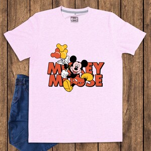 May include: A light pink t-shirt featuring a graphic of Mickey Mouse holding balloons. The text "Mickey Mouse" is displayed in orange and red. The shirt is paired with blue denim jeans.