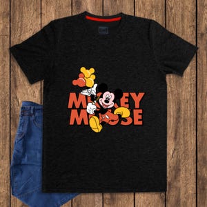 May include: Black t-shirt featuring a colorful graphic of Mickey Mouse holding balloons, with the words "Mickey Mouse" in orange. The shirt has a red collar and is paired with blue jeans. The shirt is made of a soft material.