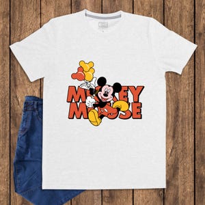 May include: A white t-shirt featuring a graphic of Mickey Mouse holding balloons. The cartoon character is in his classic red shorts, yellow shoes, and black gloves. The words "Mickey Mouse" are in orange block letters.