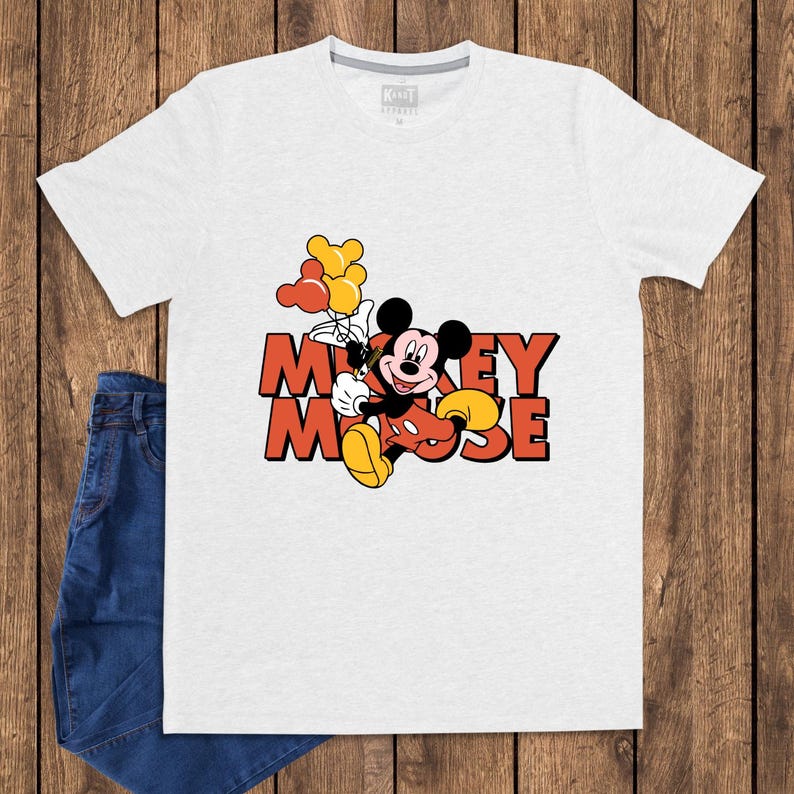May include: A white t-shirt featuring a graphic of Mickey Mouse holding balloons. The cartoon character is in his classic red shorts, yellow shoes, and black gloves. The words "Mickey Mouse" are in orange block letters.