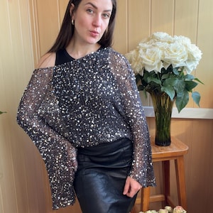 Può includere: Un top nero con paillettes e maniche lunghe e una gonna di pelle nera. Il top è ricoperto di paillettes argentate, creando un effetto scintillante. L'outfit è completato da una canotta nera sotto.