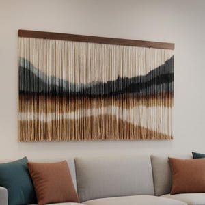 以下が含まれることがあります： 明るい灰色のソファ、ティールと錆色のクッション、濃い木製のコーヒーテーブルを備えたリビングルーム。ソファの上には風景スタイルの壁掛けがあります。部屋にはニュートラルなラグと大きな窓があります。