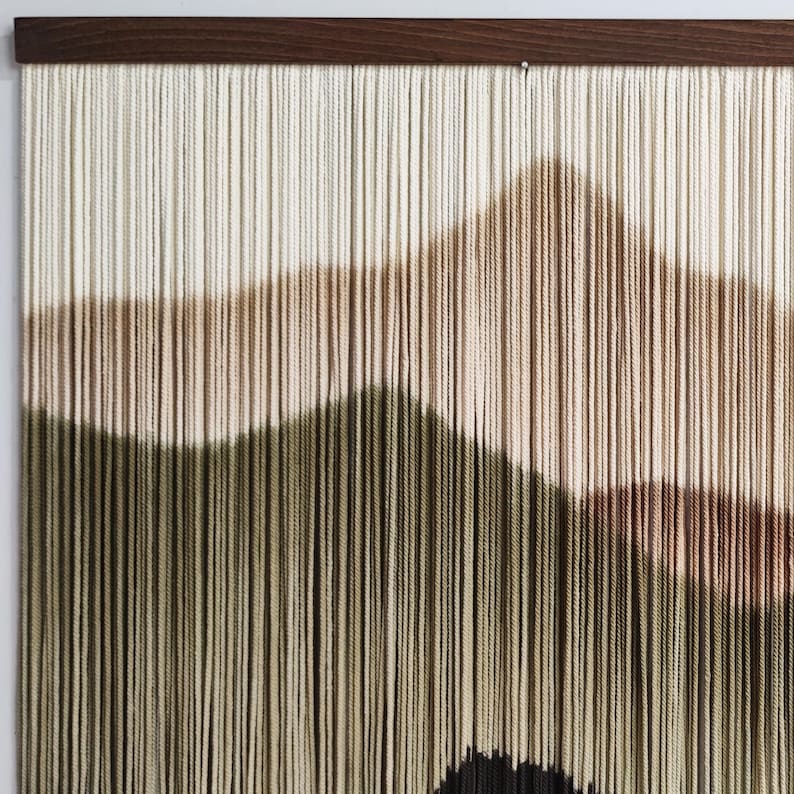 May include: A wall hanging made of yarn with a geometric design in shades of beige, brown, and green. The yarn is woven in a way that creates a textured, three-dimensional effect.