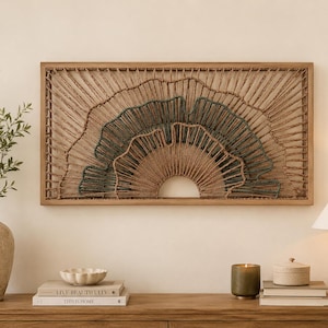 May include: A rectangular wall art piece featuring a wooden frame and a layered fibre design. The artwork consists of radiating natural tan and dark teal cord patterns arranged in a semi-circular, fan-like structure within the frame.