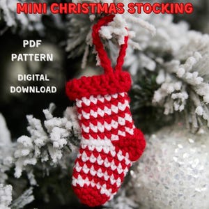 May include: A small, red and white crocheted Christmas stocking hangs from a snow-covered Christmas tree. The stocking has a red cuff and heel. Text on the image reads "Mini Christmas Stocking, PDF Pattern, Digital Download, Christmas Decoration, Bag Charm, Keychain."