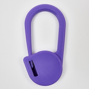 May include: A purple 3D printed plastic tool featuring a large oval handle attached to a circular base. The circular base contains a small rectangular cutout with a visible internal blade component, designed for cutting or slicing tasks.