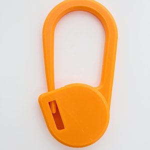 May include: A bright orange plastic carabiner with a smooth, elongated oval frame and a circular locking mechanism at the base. The locking component features a small rectangular cutout, and the entire object has a matte, textured finish.