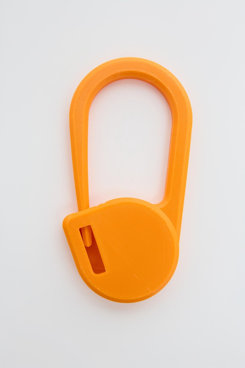 May include: A bright orange plastic carabiner with a smooth, elongated oval frame and a circular locking mechanism at the base. The locking component features a small rectangular cutout, and the entire object has a matte, textured finish.