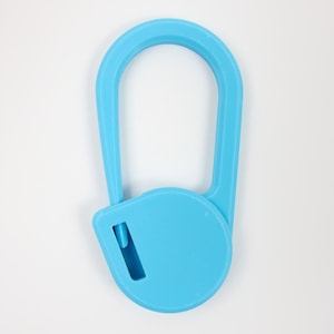 May include: A bright blue plastic safety cutter featuring a rounded, elongated handle and a circular base with a small, recessed blade slot. The tool has a textured surface finish and a simple, functional design for cutting tasks.