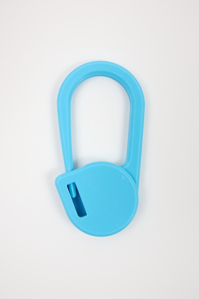 May include: A bright blue plastic safety cutter featuring a rounded, elongated handle and a circular base with a small, recessed blade slot. The tool has a textured surface finish and a simple, functional design for cutting tasks.