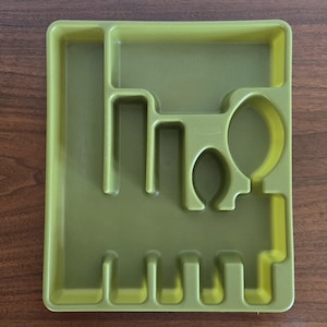 May include: A green plastic utensil tray with multiple compartments for organizing silverware. The tray has sections for forks, knives, spoons, and other kitchen tools. The tray is rectangular and has rounded corners.