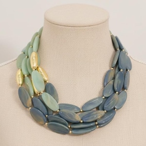 May include: A three-strand necklace with large, oval beads. The beads transition from light green to blue, with gold-colored beads interspersed. The necklace is displayed on a mannequin.