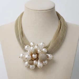 May include: A gold-toned mesh necklace with a cluster of large, white faux pearls and smaller gold-toned beads. The necklace is displayed on a mannequin, showcasing its design and texture. The central floral-like arrangement adds a touch of elegance.