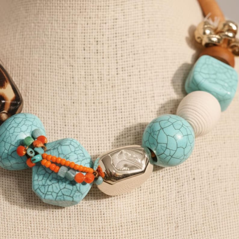 May include: A chunky necklace featuring large, turquoise-colored, cracked-effect beads, interspersed with silver, white, and wooden beads. The necklace also includes small orange and turquoise accent beads, and a leopard print bead.