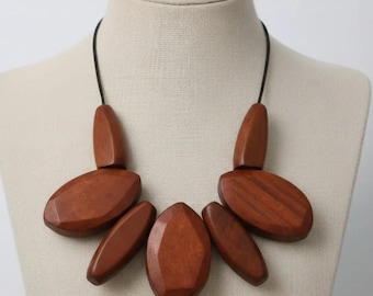 May include: A wooden necklace with a black cord. The necklace features six large, polished, brown wooden beads in various shapes, including oval and elongated forms. The beads are arranged in a symmetrical pattern.