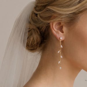 May include: Gold-toned drop earrings featuring a delicate vine design with clear, sparkling crystals. The earrings dangle gracefully, adding a touch of elegance. The earrings are a beautiful accessory for special occasions.
