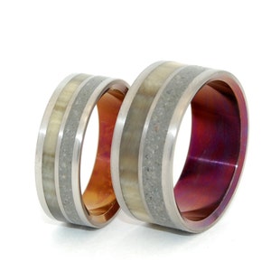 May include: Two wedding bands with a silver and gray finish. One band has a copper interior and the other has a purple interior. Both bands have a white inlay.