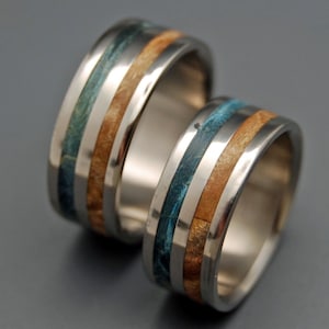 May include: Two matching wedding bands with a silver metal base and inlaid strips of blue and brown wood.