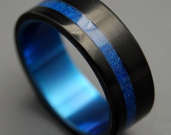 May include: A black and blue titanium ring with a blue inlay. The ring has a brushed finish and a thin blue line around the edge.