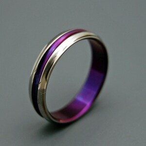May include: A silver ring with a purple and pink inlay. The ring is polished and has a smooth finish.