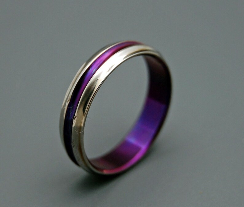 May include: A silver ring with a purple and pink inlay. The ring is polished and has a smooth finish.