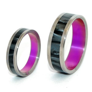 May include: Two titanium rings with a black inlay and a purple inner band. The rings are different sizes.