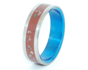 May include: A silver ring with a red band containing small white and brown flecks. The ring is also accented with a blue band.
