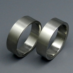 May include: Two silver metal rings, one slightly larger than the other, are stacked on top of each other. The rings are smooth and have a polished finish.