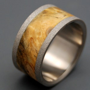 May include: A wide, silver band ring with a wood inlay. The wood is a light brown color with darker brown streaks. The band is textured and has a polished finish.