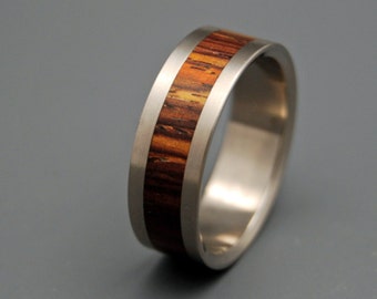 May include: A silver titanium ring with a brown wood inlay. The ring is a simple design with a smooth finish.