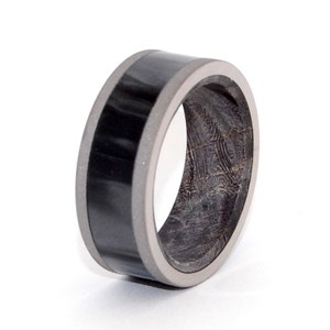 May include: A black and gray ring with a wood inlay. The ring is made of titanium and has a black carbon fiber inlay.