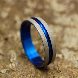 May include: A silver titanium ring with a blue inlay. The ring has a brushed finish and a single blue line running around the band.