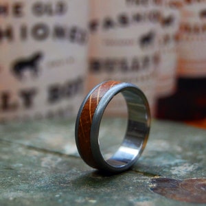 May include: A silver and wood ring with a brown wood inlay. The ring is made of stainless steel and has a brushed finish.