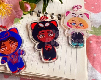 May include: Three colorful cartoon character keychains with different animal hoods. The first keychain features a blue hooded character with a red spider design. The second keychain features a black hooded character with a red spider design. The third keychain features a white hooded character with a black spider design.