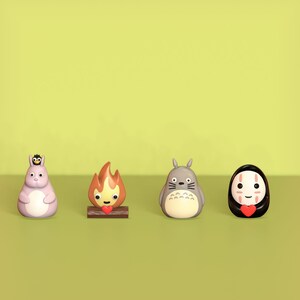 May include: Four small figurines of characters from the animated film 'My Neighbor Totoro' and 'Spirited Away'. The figurines are made of plastic and are painted in various colors. The characters include Totoro, a soot sprite, No Face, and a fire spirit.