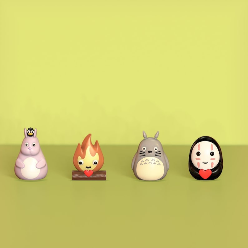 May include: Four small figurines of characters from the animated film 'My Neighbor Totoro' and 'Spirited Away'. The figurines are made of plastic and are painted in various colors. The characters include Totoro, a soot sprite, No Face, and a fire spirit.