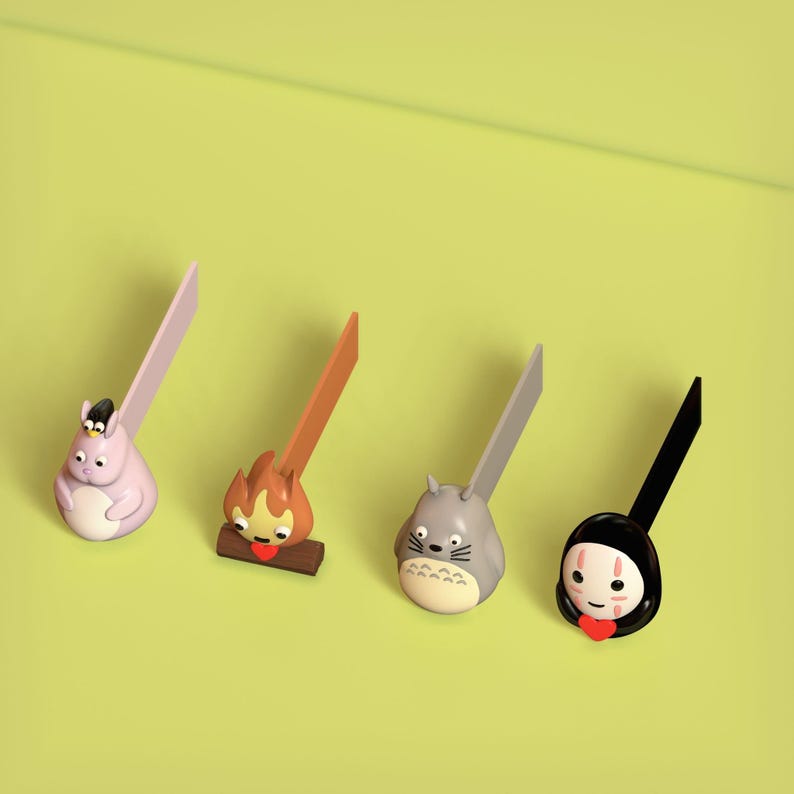 May include: Four colorful bookmarks featuring characters from popular animated films. The bookmarks are made of plastic and have a flat, rectangular shape. The characters include a pink Totoro, a brown fire spirit, a gray Totoro, and a white No Face.